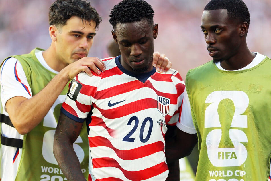 Folarin Balogun (c.) is consoled by teammates Giovanni Reyna (l.) and Timothy Weah (r.) after receiving a red card.