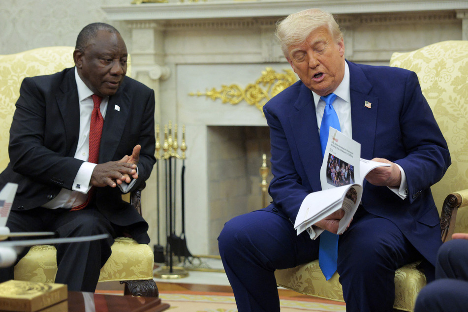 President of South Africa Cyril Ramaphosa (l.) looks on as US President Donald Trump (r.) displays articles he says report violence against white South Africans in the Oval Office of the White House on May 21, 2025 in Washington, DC.