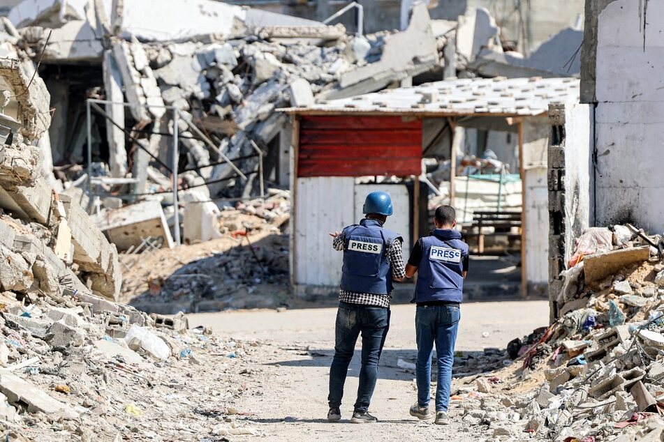 Journalists film while standing before destroyed buildings in the Jabalia camp for Palestinian refugees in the northern Gaza Strip.