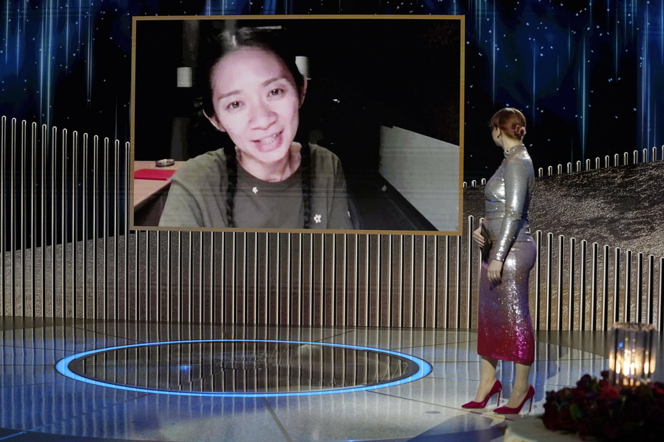 Chloé Zhao (l.) takes the win as best director for Nomadland. Bryce Dallas Howard announces her nomination on-stage.