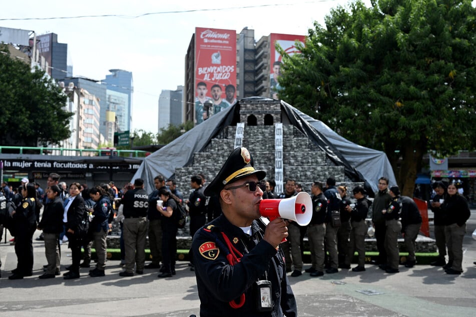 A member of the Secretariat of Citizen Security uses a megaphone to give instructions to personnel evacuated from several buildings following a preventive evacuation in Mexico City on Friday, after a 7.3-magnitude earthquake struck southern Mexico and parts of Central America.