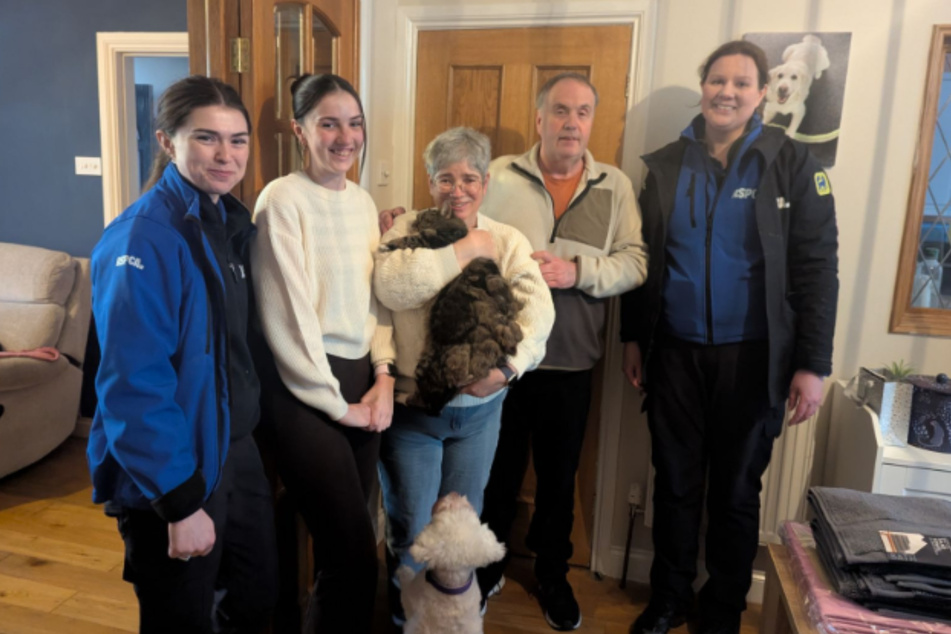 Mandy Davis holds Alfie the cat in her arms while her family and two of the rescuers smile at the camera.