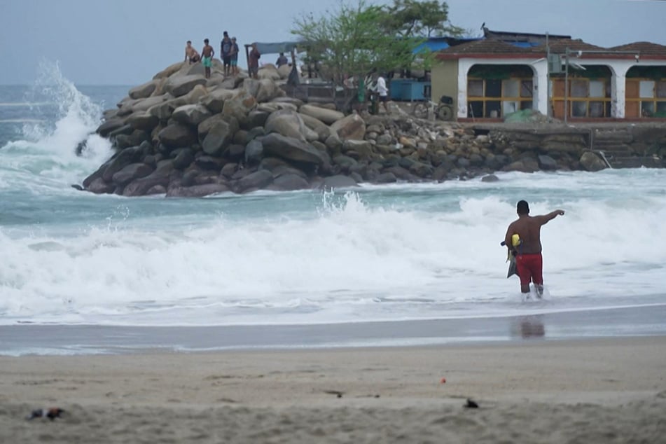 People stand at the beach of Puerto Escondido as Hurricane Erick approaches Mexico's Pacific coast.