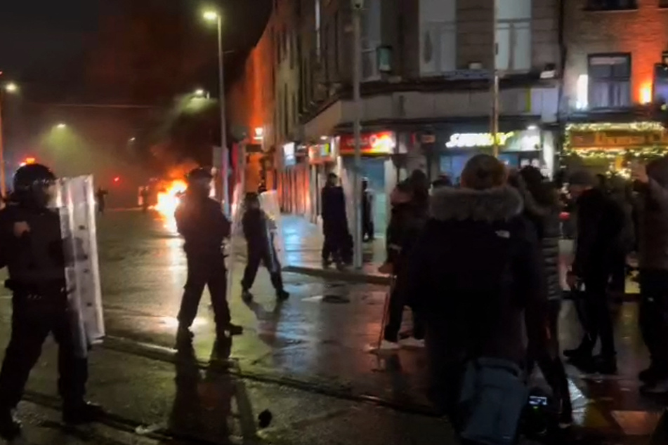Irish Garda riot police form a cordon around a burning police car on Thursday as a crowd forms.