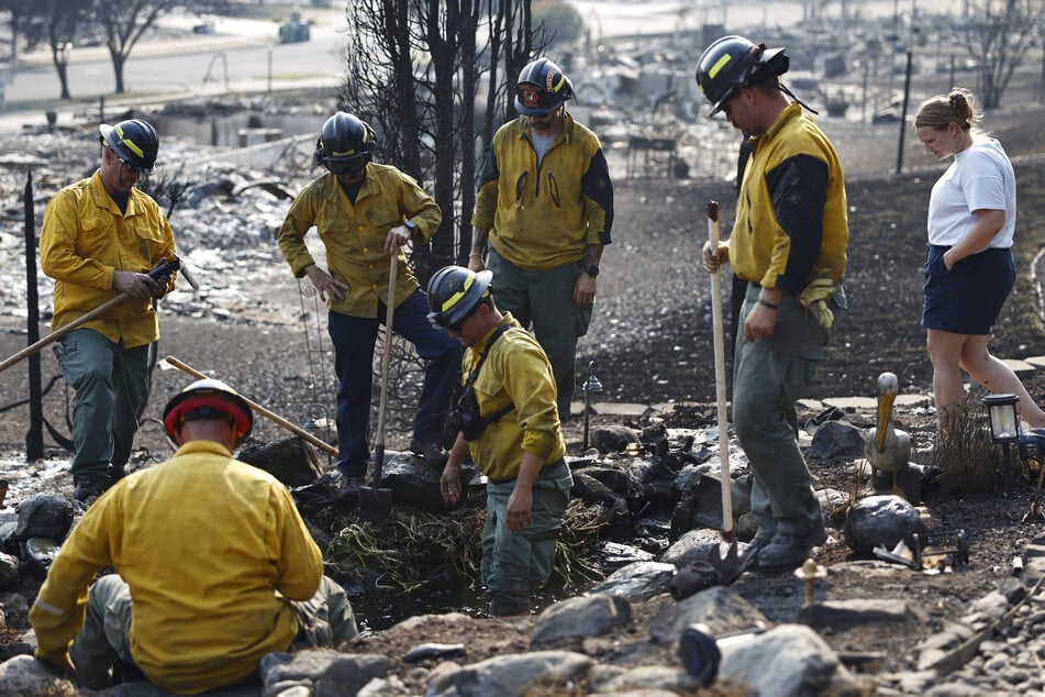 Firefighters work to rescue surviving fish from a pond at a resident's home, which was destroyed in the Old Trails Fire on Wednesday in Spokane, Washington.