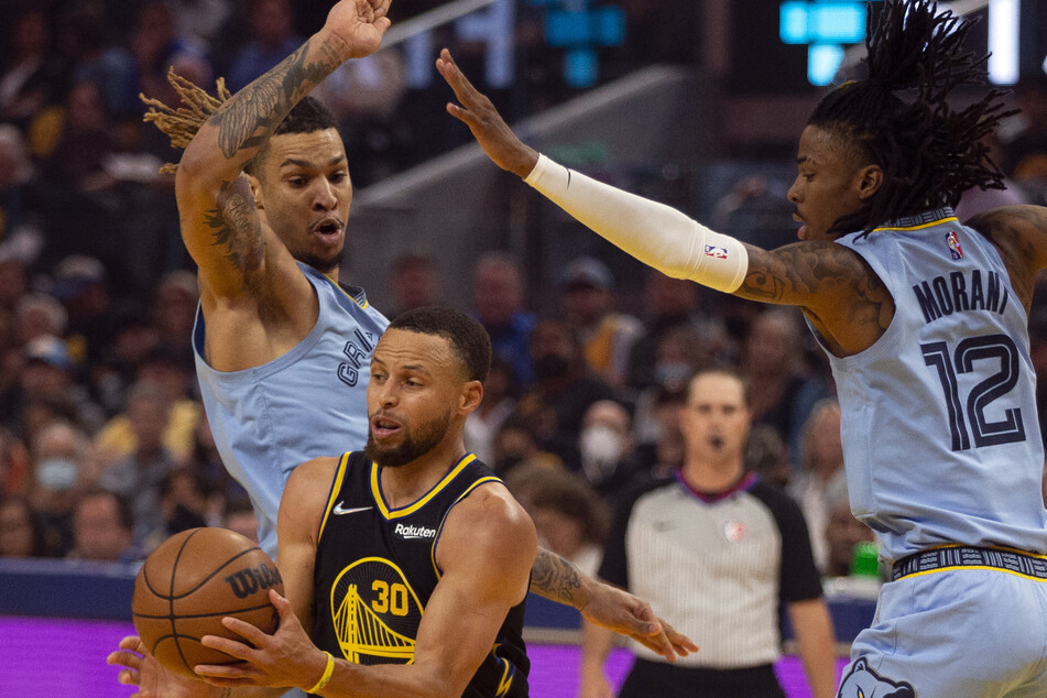 Warriors guard Stephen Curry (c.) drives between Grizzlies forward Brandon Clarke and guard Ja Morant.