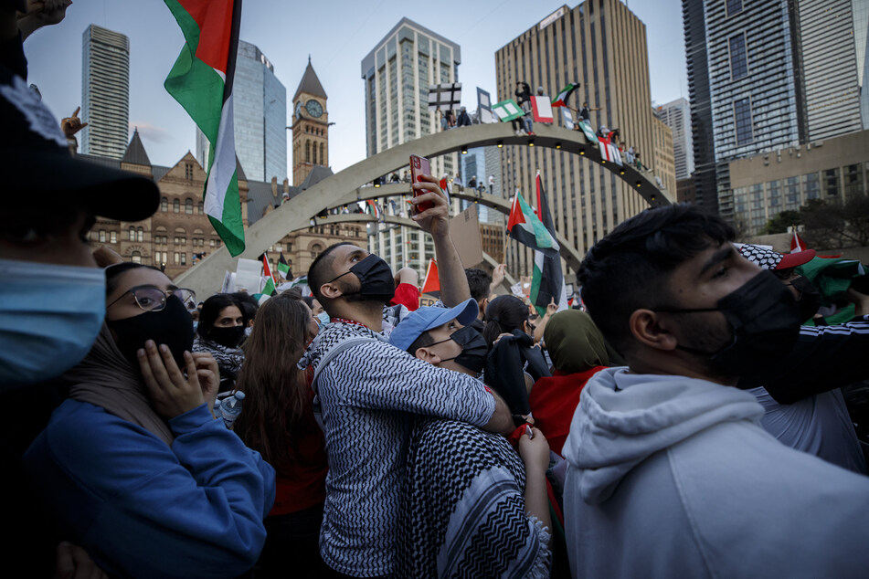 People film, chant, and wave flags during a demonstration in support for the people of Palestine, at Toronto City Hall in Ontario, Canada.