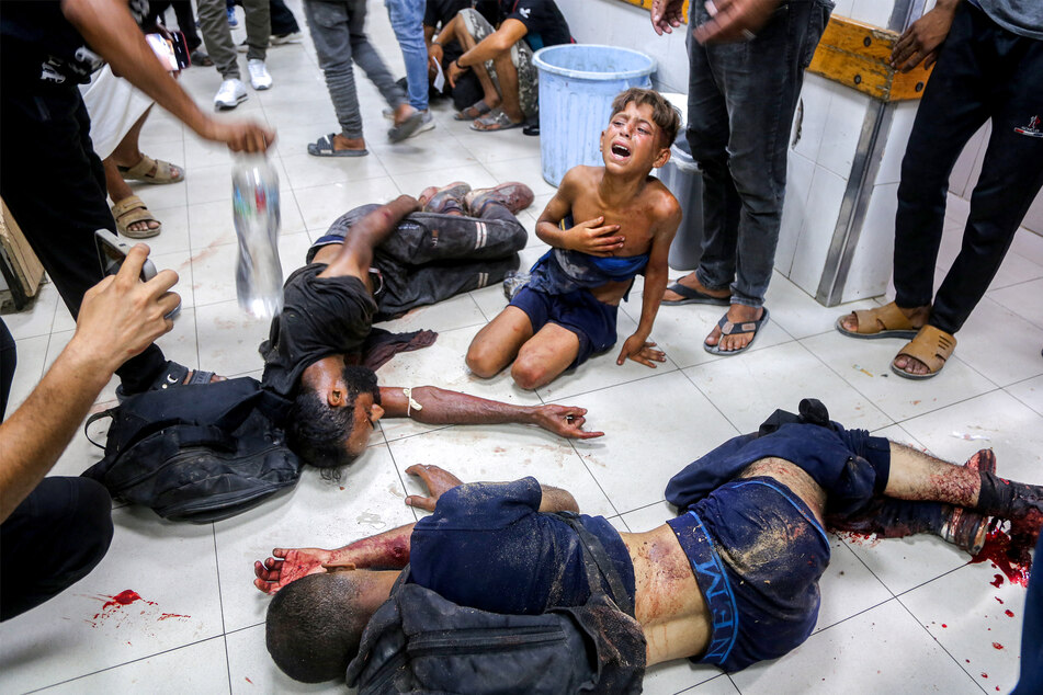 An injured boy reacts as he sits on the ground by other men who were all wounded while previously queueing for aid, at Nasser Medical Complex in Khan Younis in the southern Gaza Strip on July 20, 2025.