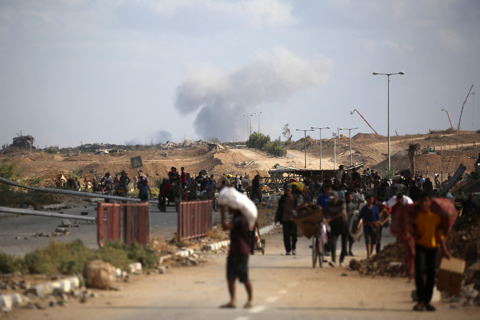 A plume of smoke rises in the background as Palestinians return from a food distribution point run by the US and Israeli-backed Gaza Humanitarian Foundation, near the Netsarim corridor in the central Gaza Strip, on October 5, 2025.
