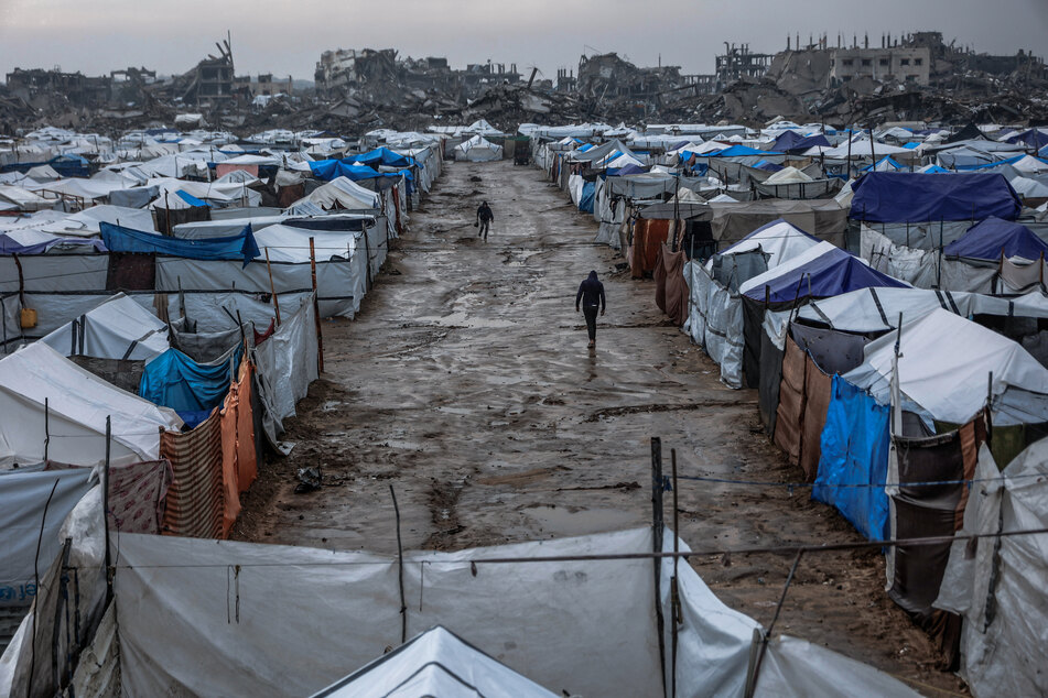 Men walk along a muddy alley at a makeshift camp sheltering displaced Palestinians after heavy rains in the Zeitoun neighbourhood of Gaza City on December 11, 2025.