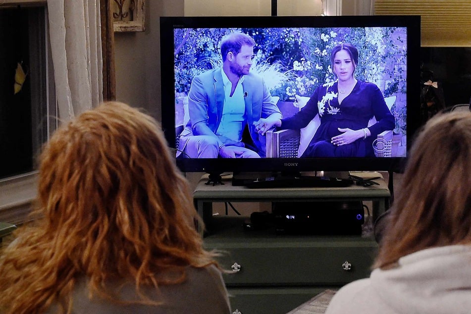 This photo shows people watching a TV conversation between Prince Harry, Meghan Markle, and Oprah Winfrey on March 7, 2021.