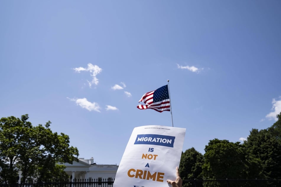 A protester holds a sign reading "Migration Is Not a Crime" outside the White House in Washington DC.