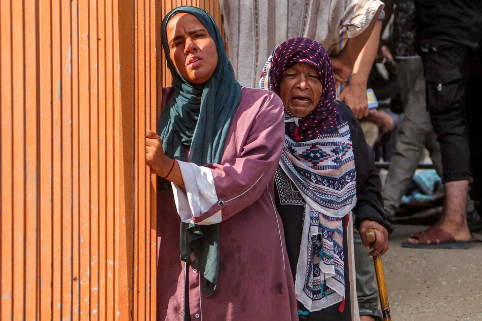 Women are pictured near mourners praying by the bodies of victims who were killed the previous day by Israeli bombardment as they lie outside during the funeral at Nasser Medical Complex in Khan Younis on July 20, 2025.