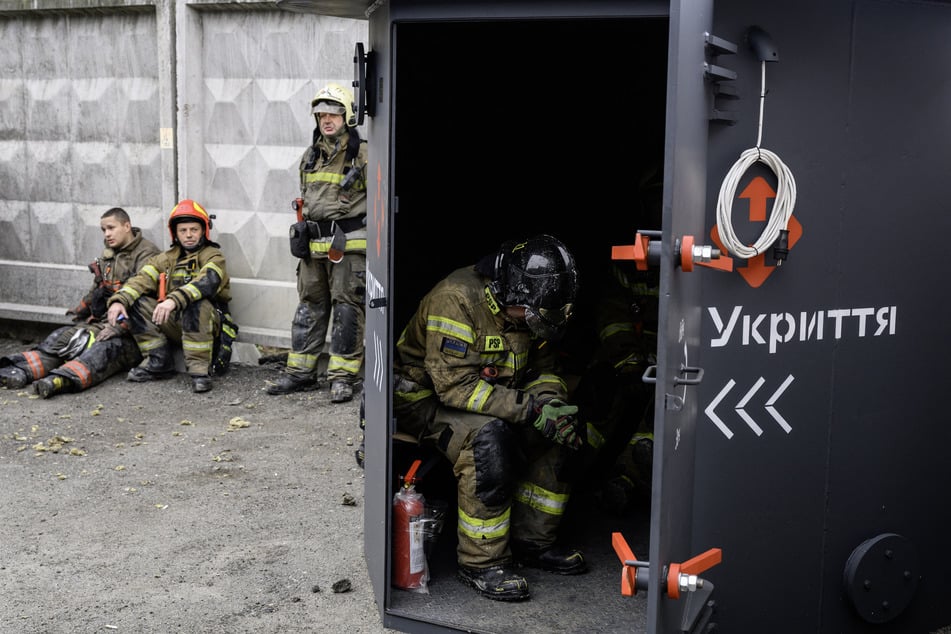 Ukrainian rescuers take a break at the site of a shopping center damaged following a missile strike in Kyiv on October 22, 2026.