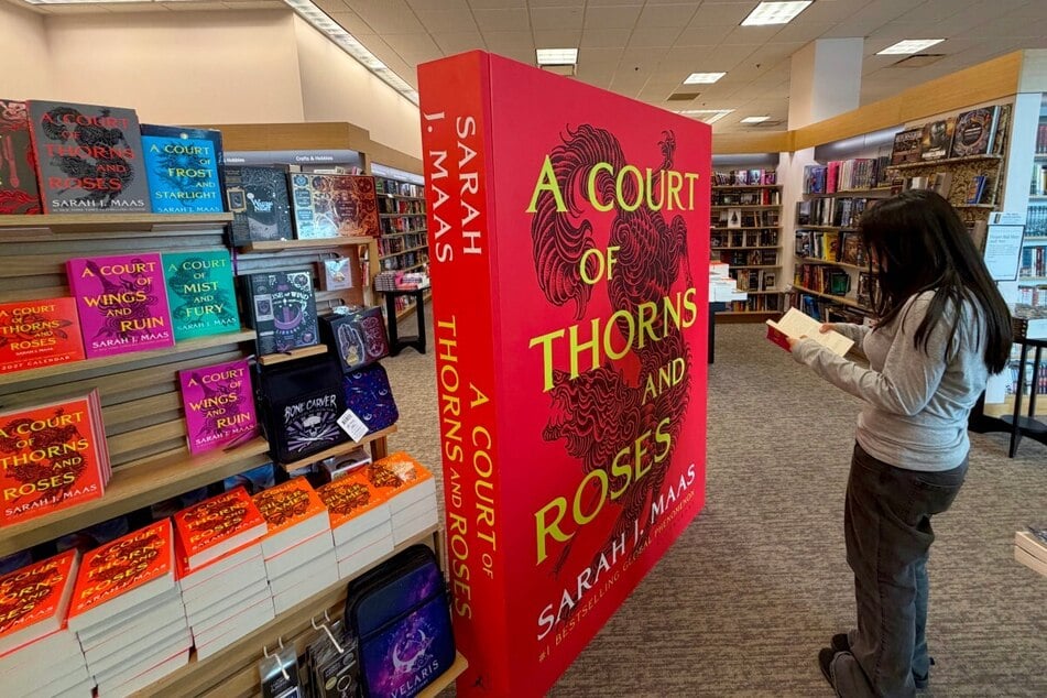 A girl reads a Sarah J. Maas book next to a large promotional display of her new release, A Court of Thorns and Roses, at a bookstore in Los Angeles on October 23, 2026. The book comes after a five-year hiatus.