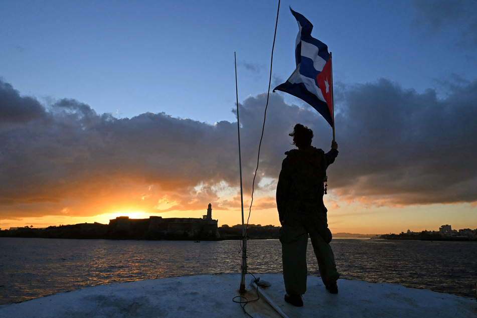 An activist waves a Cuban flag on board the vessel Maguro as it arrives from Mexico with humanitarian aid as part of the Nuestra America convoy, docking at the port of Havana on March 24, 2026.