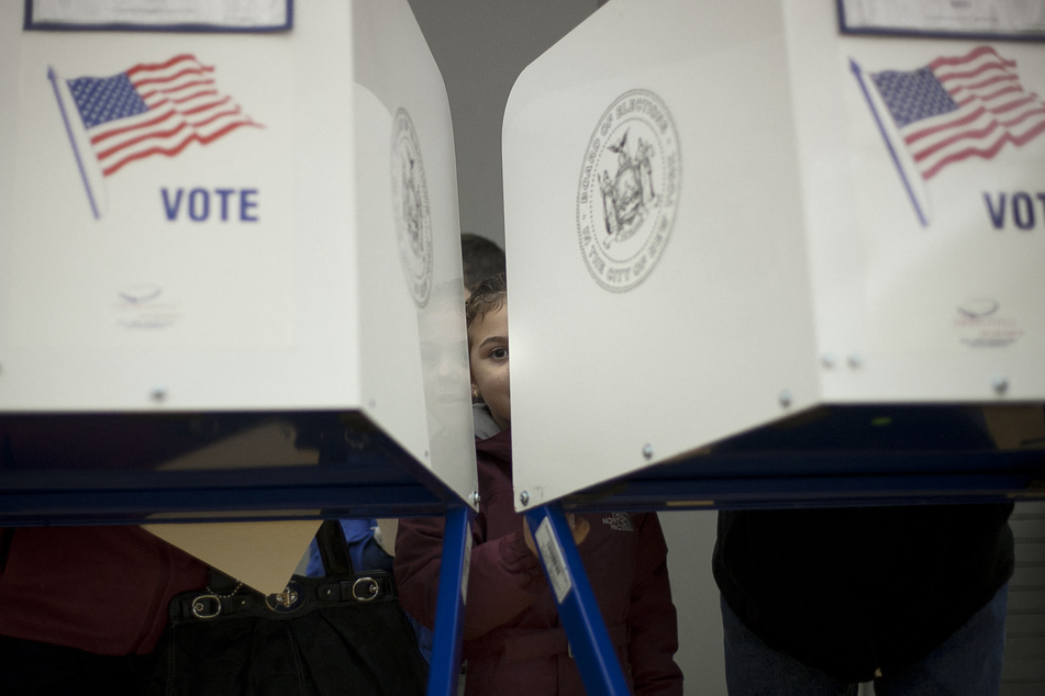 A young girl looks out from a privacy booth as her parents vote in the Staten Island borough of New York City.