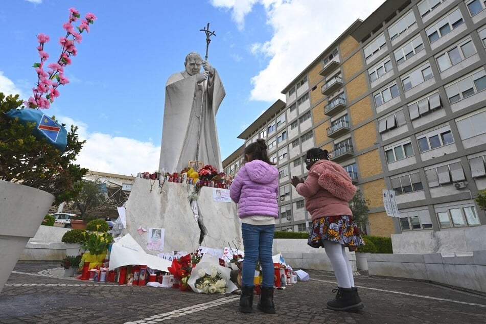 Children pray for Pope Francis in front of the statue of John Paul II outside the Gemelli University Hospital.