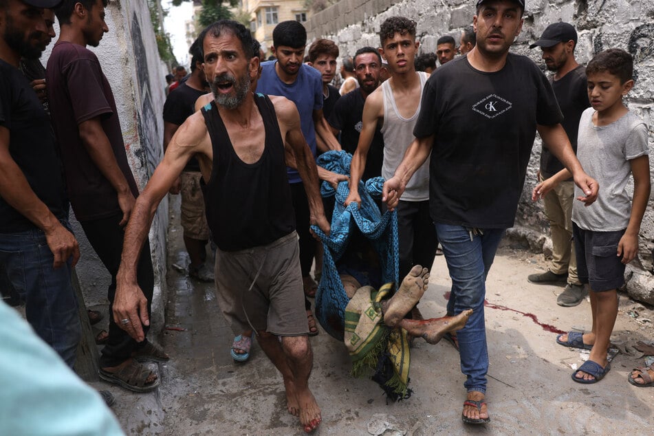 People recover the body of a Palestinian man, killed in an Israeli strike, west of Gaza City on August 12, 2025.