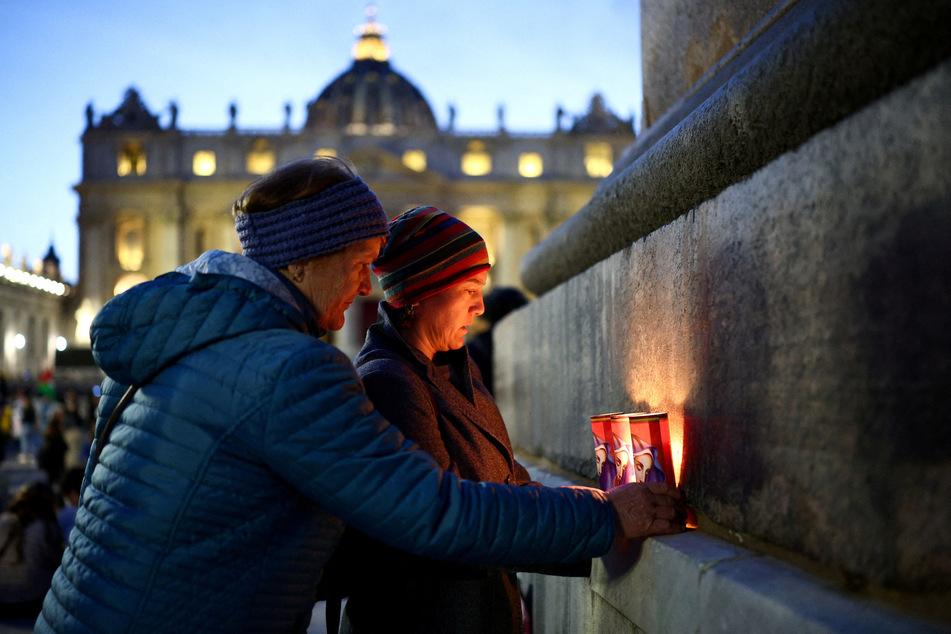 People place candles at the obelisk following the death of Pope Francis in St. Peter's Square at the Vatican.