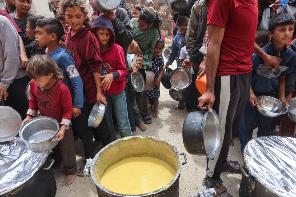 Palestinian children line up to get a ration of hot food from a charity kitchen set up at the Islamic University campus in Gaza City on May 12, 2025.