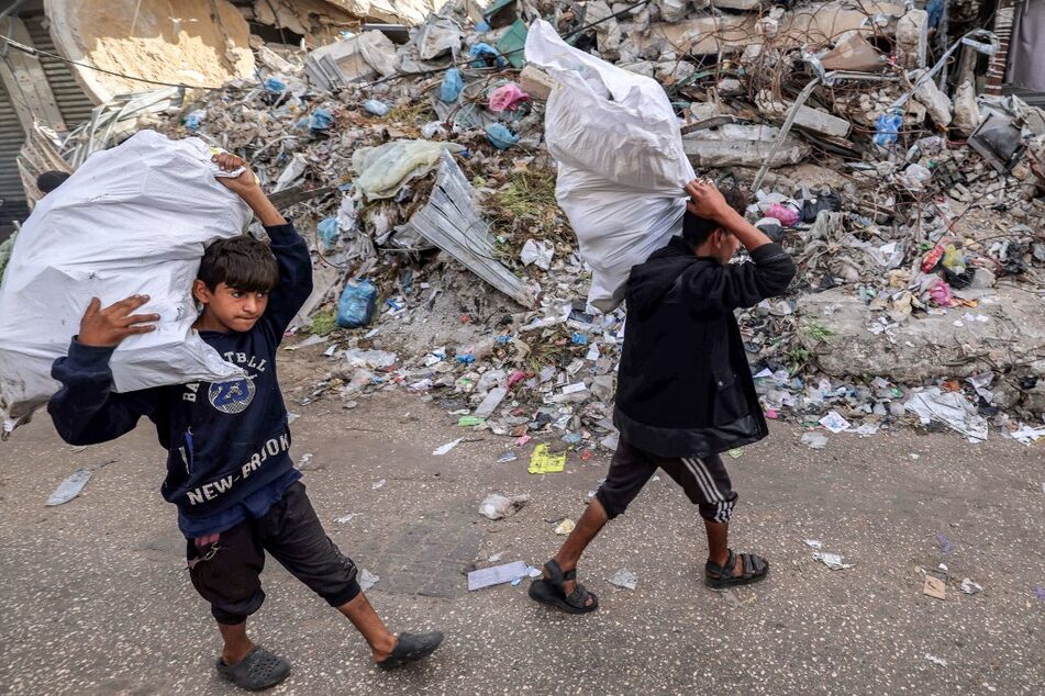 Boys walk with sacks of collected wood and plastic past the rubble of a collapsed building in Rafah in the southern Gaza Strip on April 23, 2024.