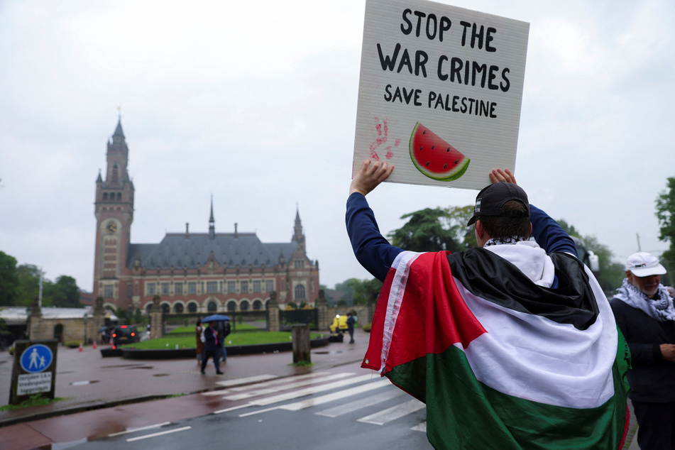 A protester draped in a Palestinian flag holds up a sign reading "Stop the War Crimes, Save Palestine" outside the International Court of Justice in The Hague, Netherlands.