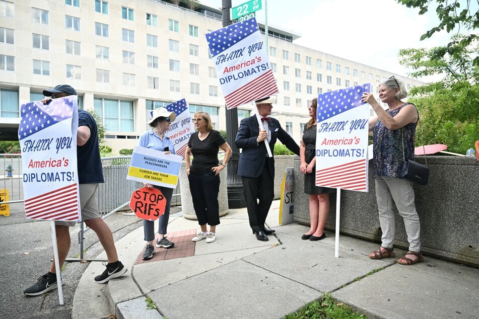 People hold signs outside the US State Department in Washington, DC, on Friday in support of laid-off diplomats.
