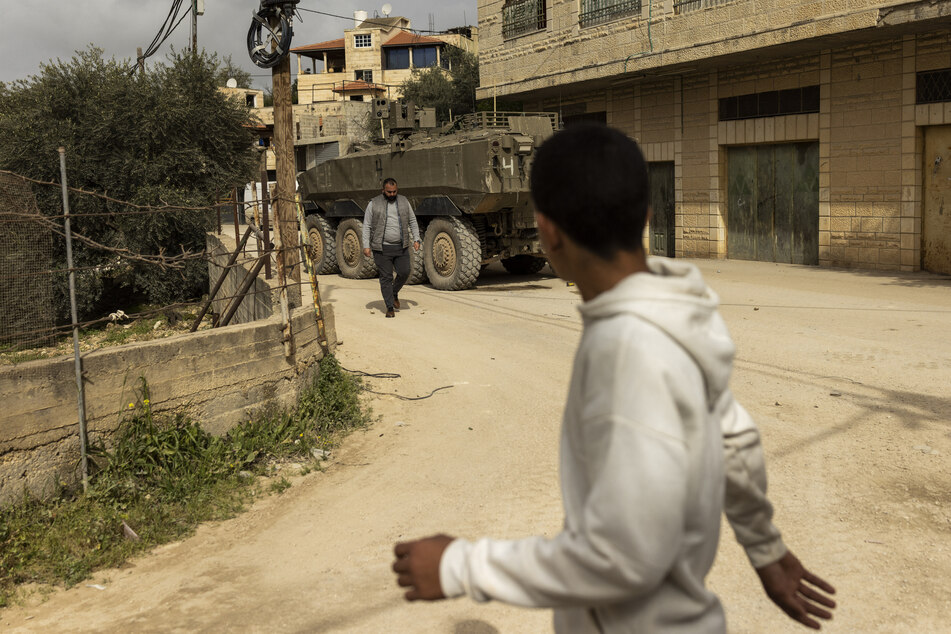 Palestinian men walk past an Israeli armored vehicle during a military raid in al-Yamun town west of Jenin in the occupied West Bank on February 17, 2026.