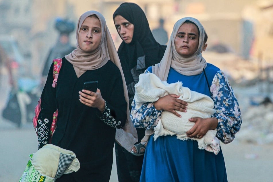 Several displaced Palestinian woman, including one holding a baby wrapped in a blanket, evacuate Khan Younis.
