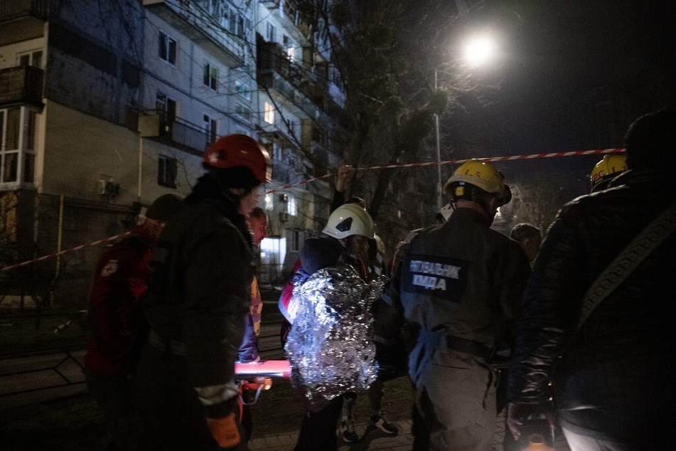 Rescuers and paramedics evacuate an elderly woman near a damaged residential building following a drone attack in Kyiv on March 23, 2025.