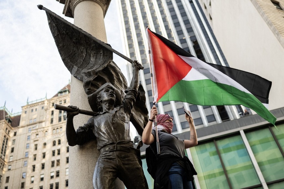 A demonstrator stands on The Admission Day Monument and waves a Palestinian flag during the "No on APEC" protest.