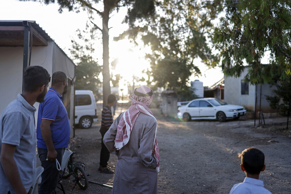 Palestinians stand at the entrance of the Bedouin community of Dar Abu Faza as Israeli settlers pass through with their herd of livestock, on the outskirts of the Israeli-occupied West Bank village of Taybeh, on June 9, 2026.