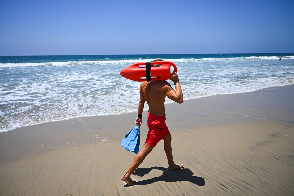 Los Angeles County Lifeguard Maximus Oberto carries a rescue can while patrolling the shoreline and monitoring swimmers in the Pacific Ocean in Manhattan Beach, California, on July 30, 2026.