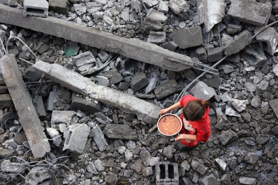 A Palestinian girl carries a portion of food as she makes her way amidst the debris at the site of an Israeli strike in Jabalia on January 1, 2025.