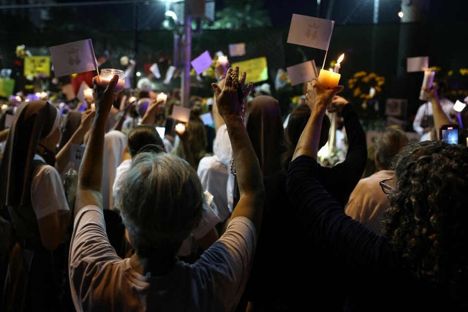 People lift their hands during a prayer at the memorial site for victims of the Surfside condo collapse.