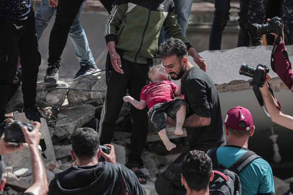 A Palestinian man evacuates a child from the rubble of a bombed building in Gaza.
