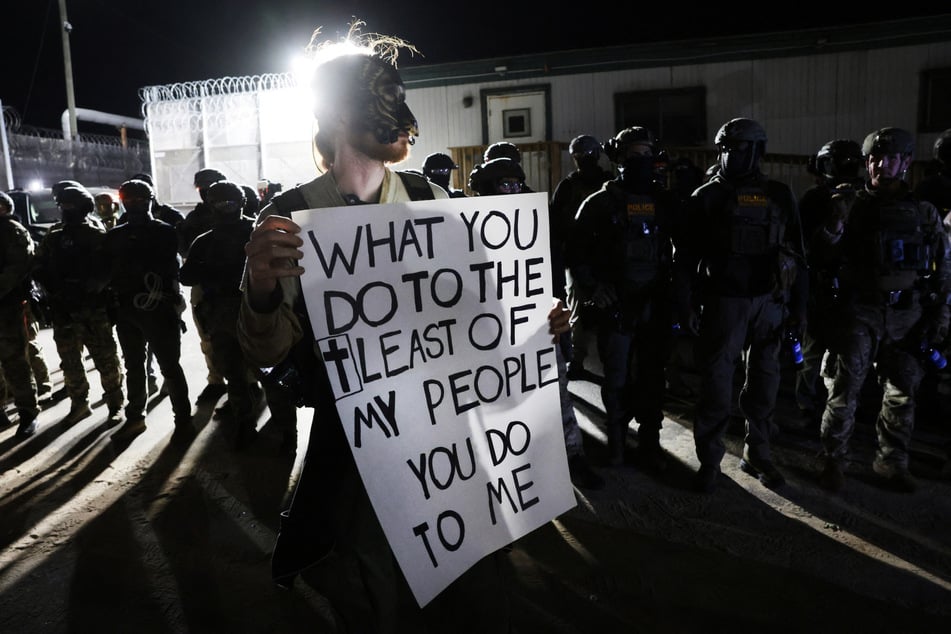 A protester, flanked by US Immigration and Customs Enforcement agents, holds a sign denouncing the Trump administration's immigration policy in Newark, New Jersey.