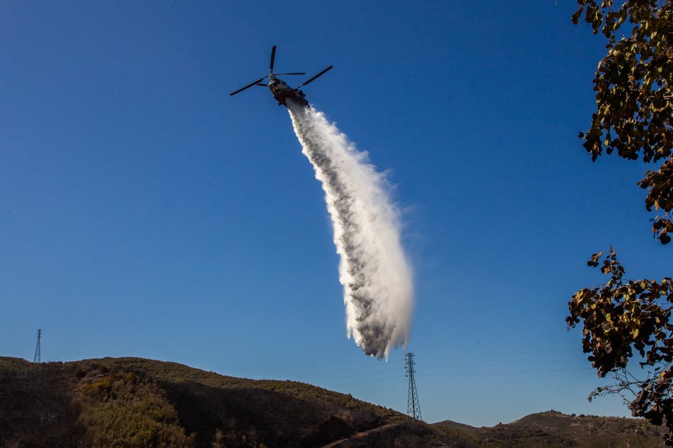 A firefighting helicopter drops water on a hillside at the Bryson Fire in Malibu, California, on October 16, 2026.