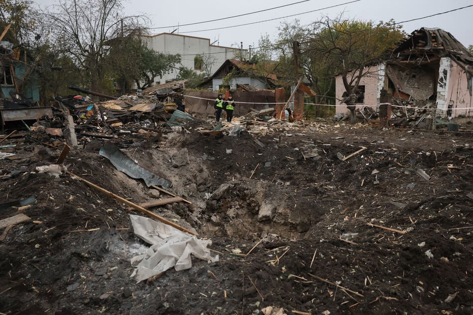 Ukrainian police officers stand next to a crater at the site of a missile strike in Kyiv on October 22, 2026.
