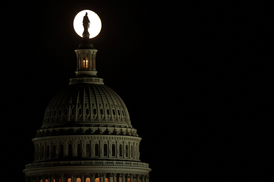 The moon creates a silhouette of the Statue of Freedom atop the US Capitol during a continuing partial federal government shutdown on October 8, 2025.