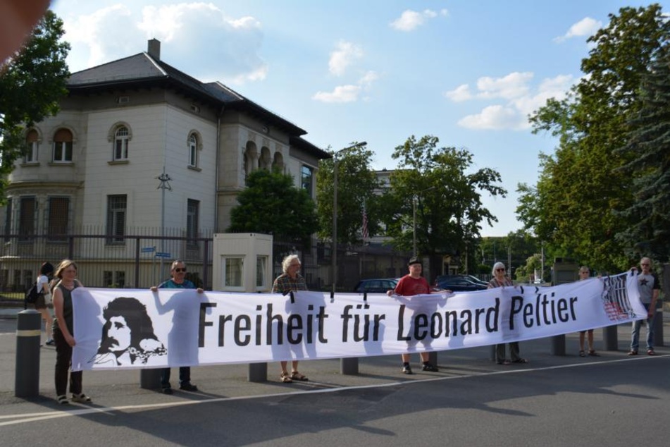 German activists hold a large banner reading "Freiheit für Leonard Peltier" ("Freedom for Leonard Peltier") outside the US Consulate in Leipzig in Summer 2024.