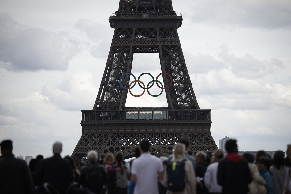 People stand in front of the Eiffel Tower, decorated with the Olympic rings for the upcoming Paris 2024 Olympic Games, in Paris on Friday.