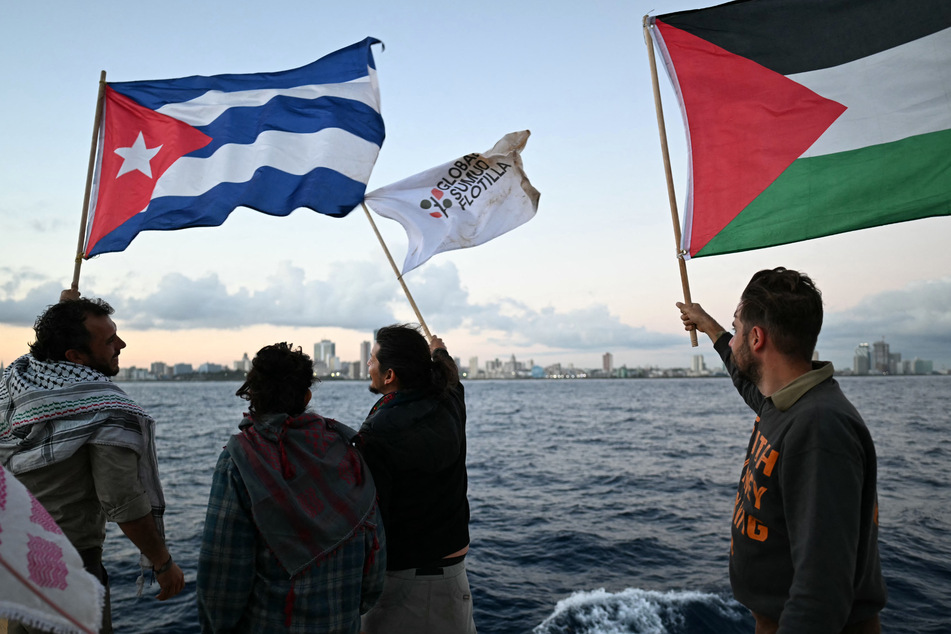 Activists wave Cuban and Palestinian flags on board the vessel Maguro as it arrives from Mexico with humanitarian aid as part of the Nuestra América convoy.