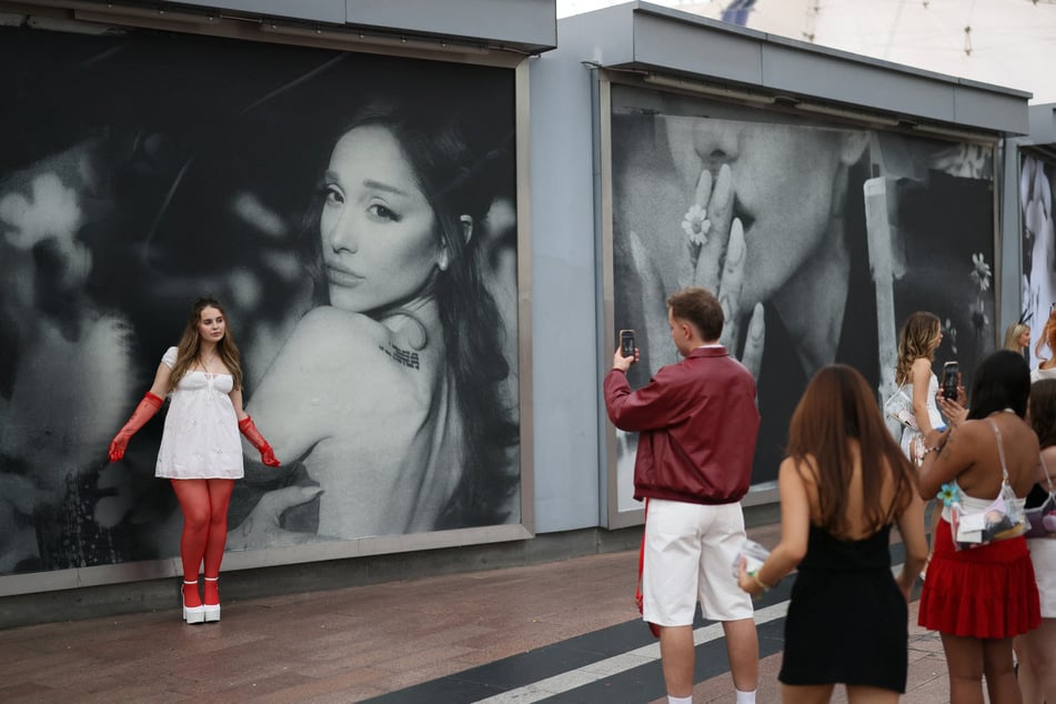 Fans take pictures in front of a billboard as they gather ahead of the opening night of the London leg of Ariana Grande's The Eternal Sunshine Tour.