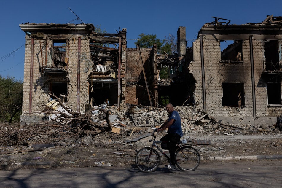 A man rides a bicycle past a damaged residential building in Novodonets'ke, in the Donetsk region, on September 14, 2025.