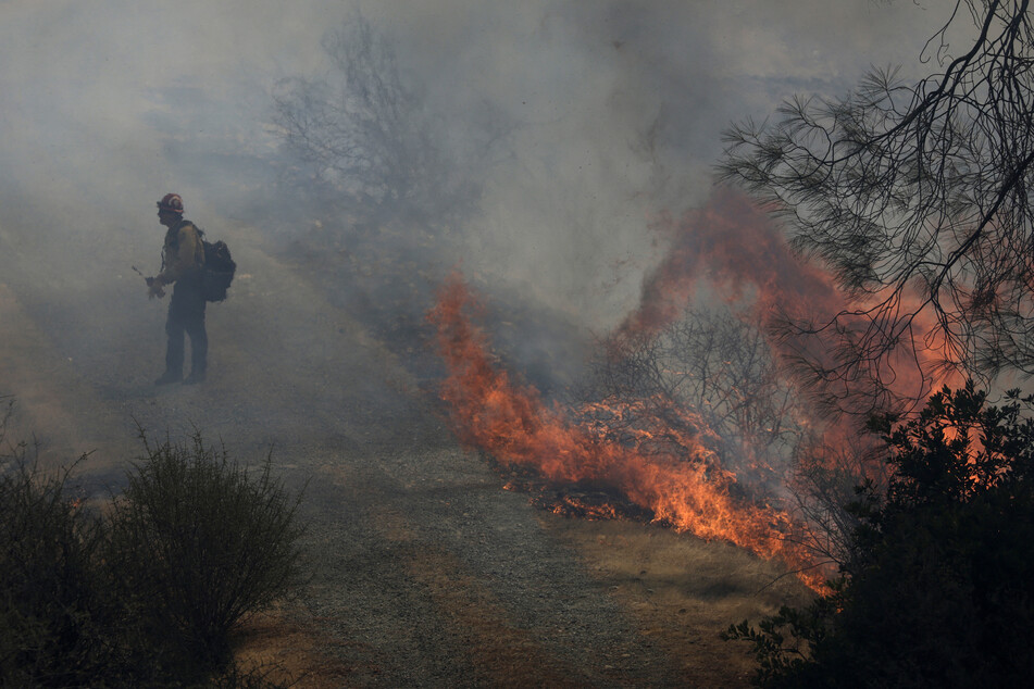 A Cal Fire firefighter walks by flames from the 6-5 Fire in the TCU September Lightning Complex on Wednesday near Chinese Camp, California.