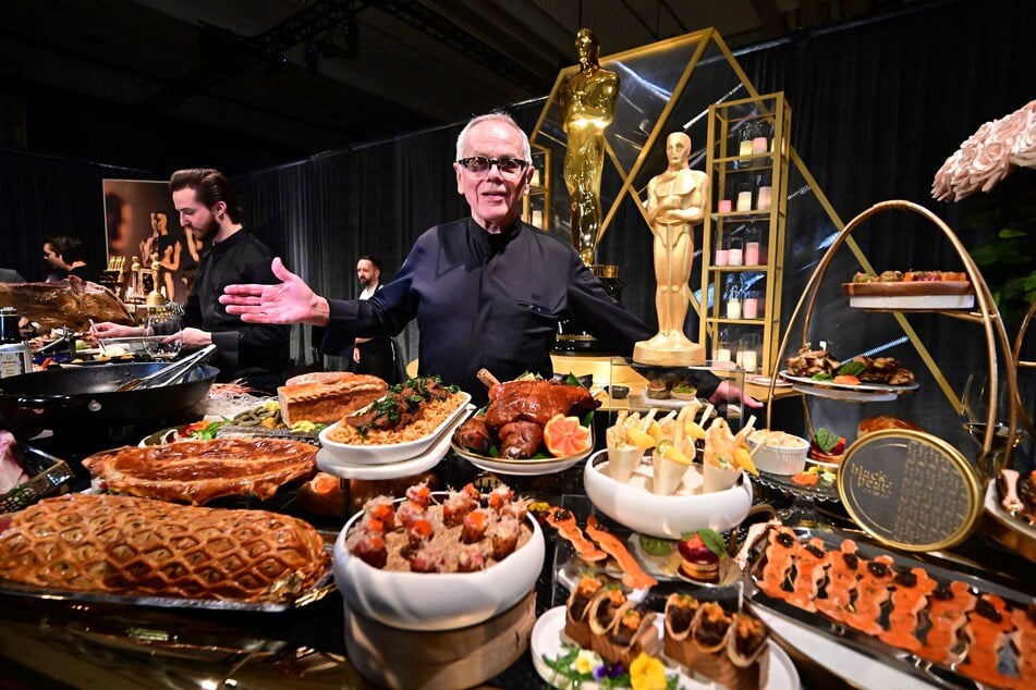 Chef Wolfgang Puck gestures from behind a display of food in Hollywood, California, on Tuesday during a media preview of the food, beverages, and decor for the Governors Ball, the Academy's official post-Oscars celebration, which will immediately follow the 97th Oscars ceremony on March 2.