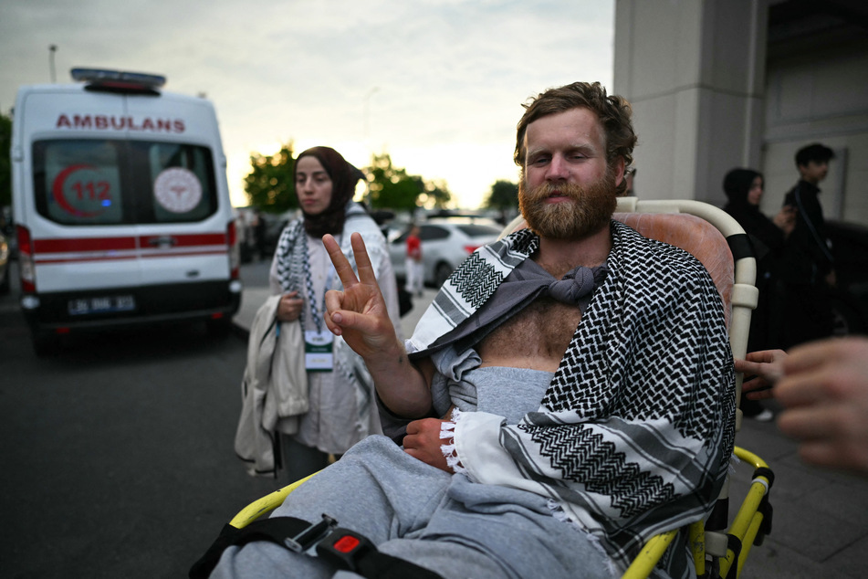 A member of the Global Sumud Flotilla gestures the V-sign as he is brought out of a terminal on a wheelchair following the group's arrival at Istanbul Airport on May 21, 2026.