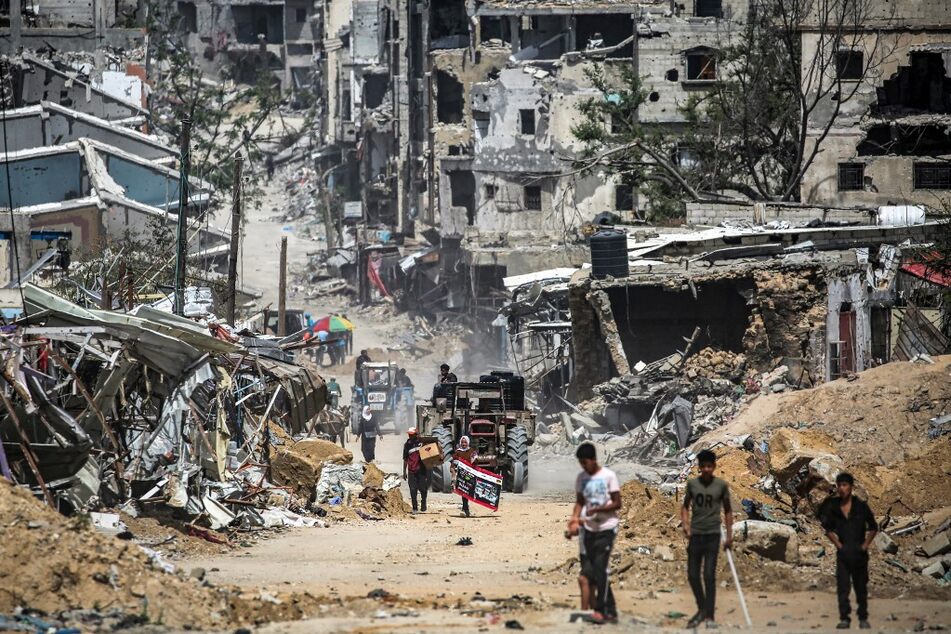 A tractor pulling a cart loaded with cisterns moves past destroyed buildings in Khan Younis in the southern Gaza Strip.